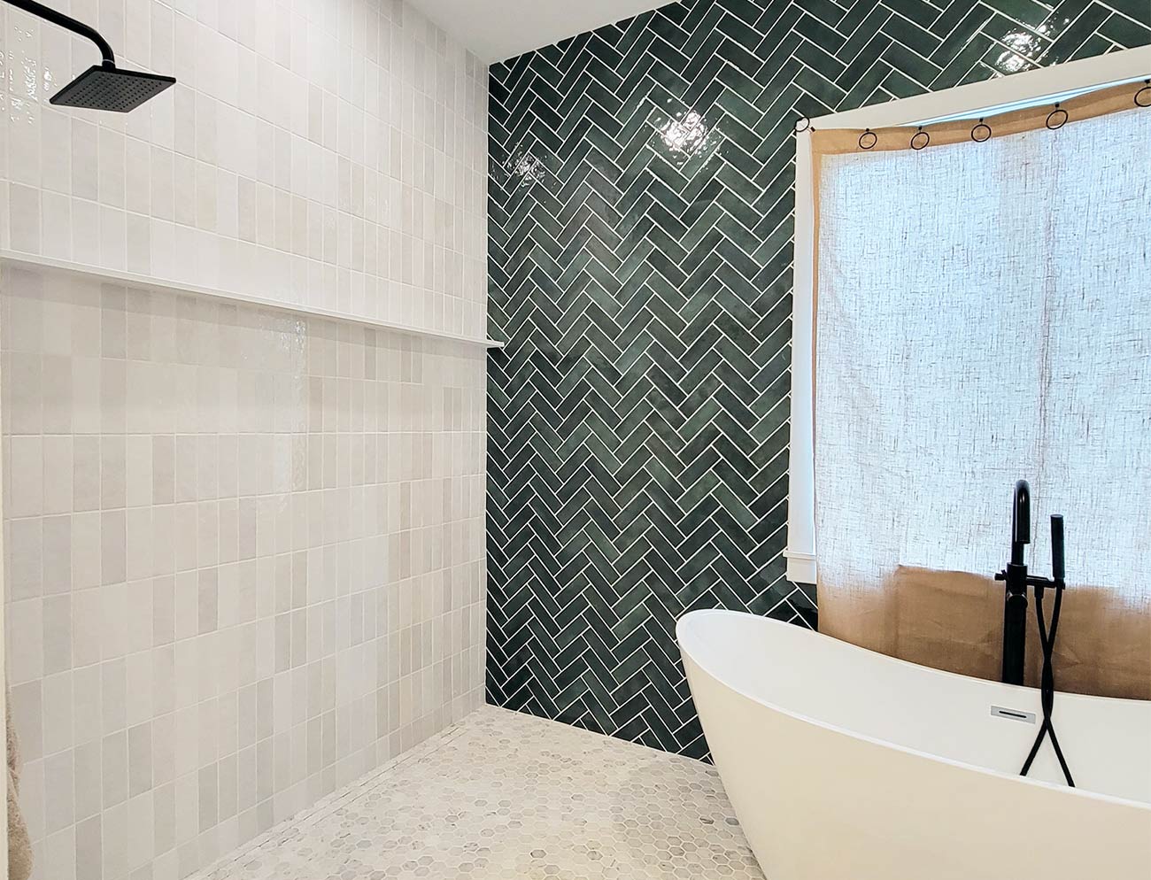 Modern bathroom with green herringbone wall tile and white hexagonal floor tile with white bathtub